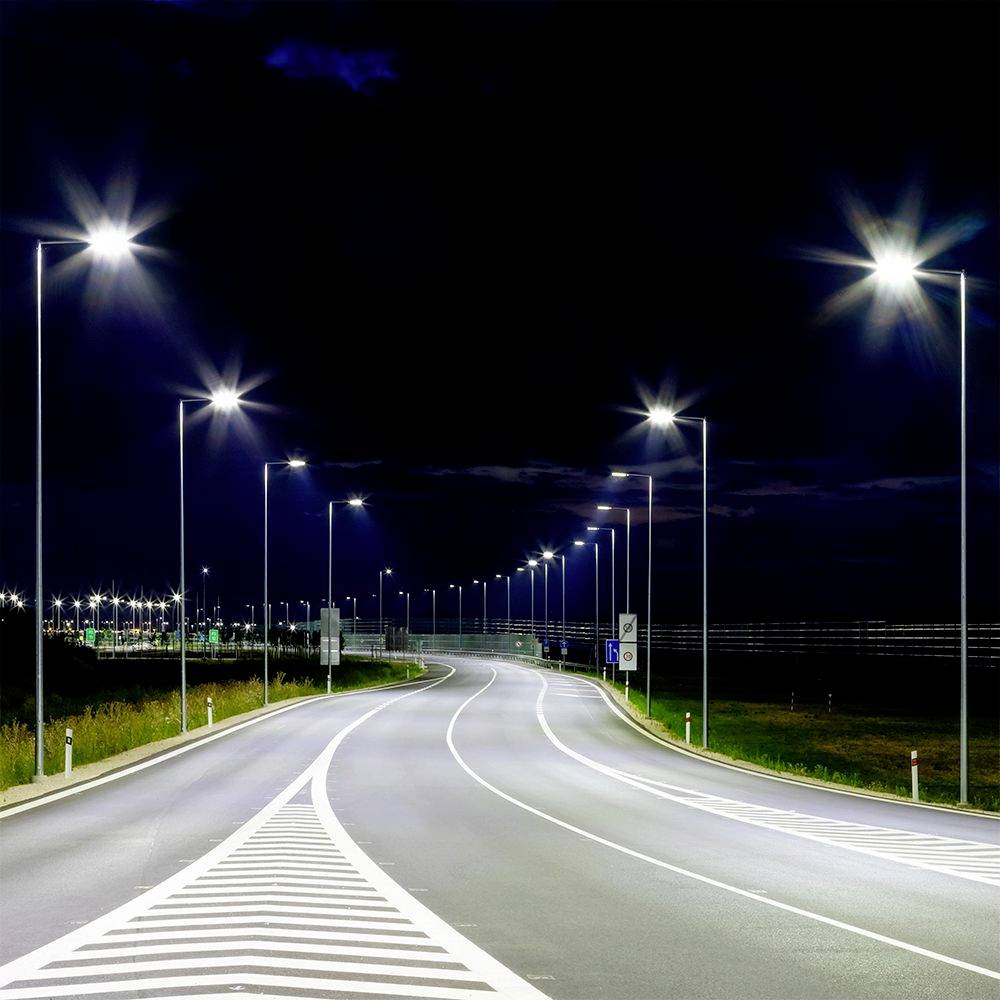 A nighttime road scene with streetlights illuminating a curving highway, highlighting lane markings. The sky is dark, and the road is empty.