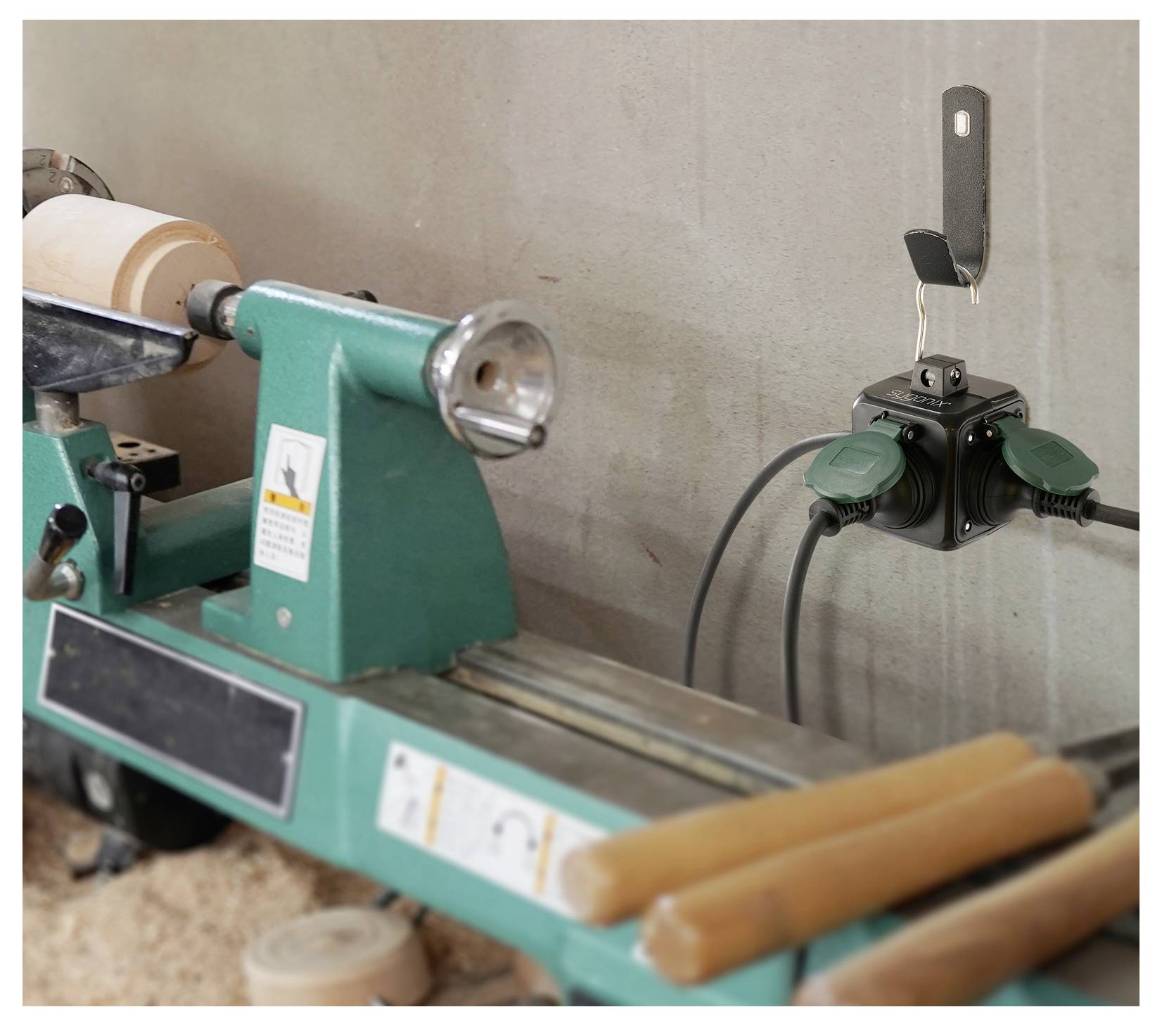 'A lathe machine and power outlet with tools on wall suggest a woodworking setup.'