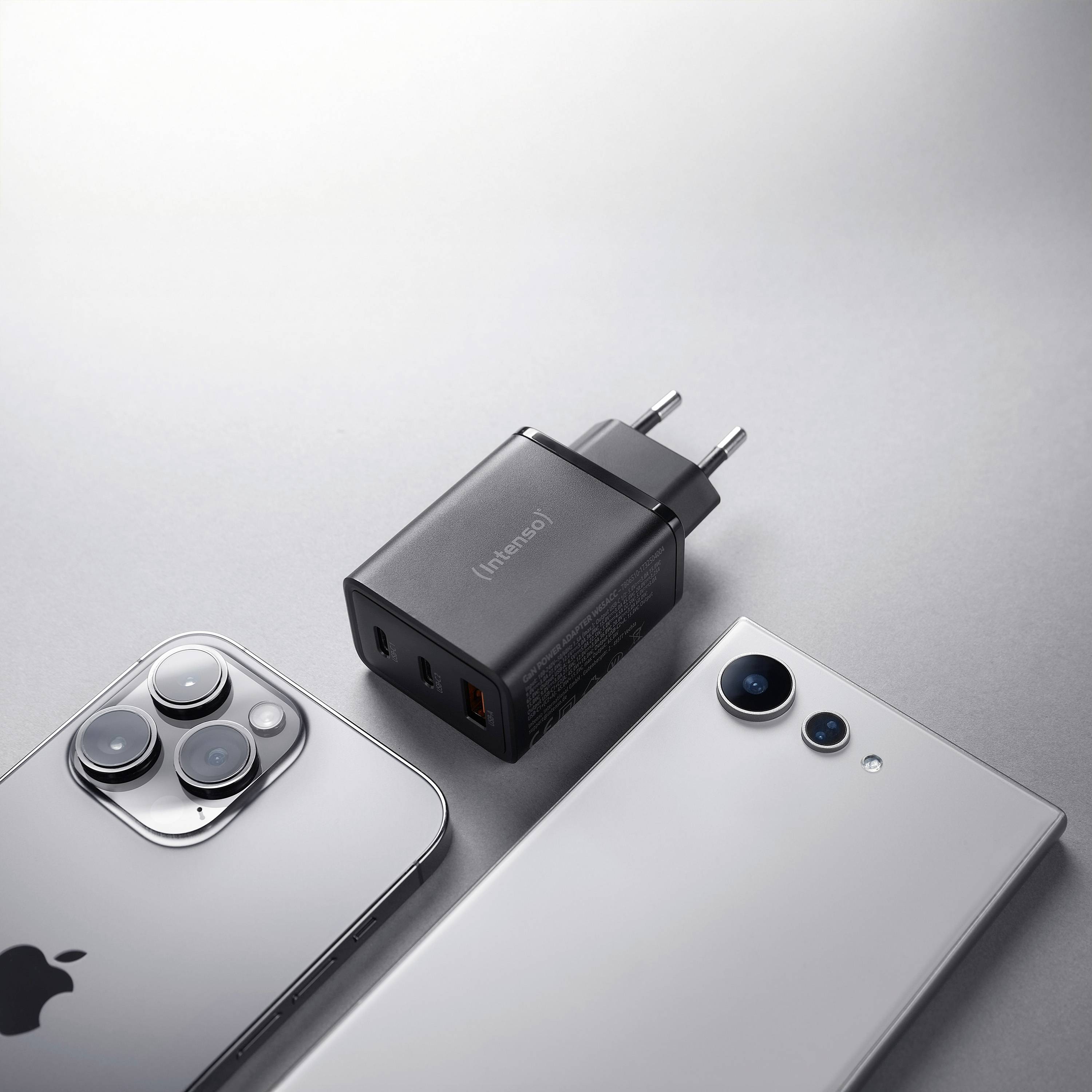 Two smartphones, one silver with three cameras and one white with two cameras, lie beside a black USB charger with multiple ports.