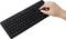 A person's hand uses the trackpad on a slim black wireless keyboard with a numeric keypad on the right side.