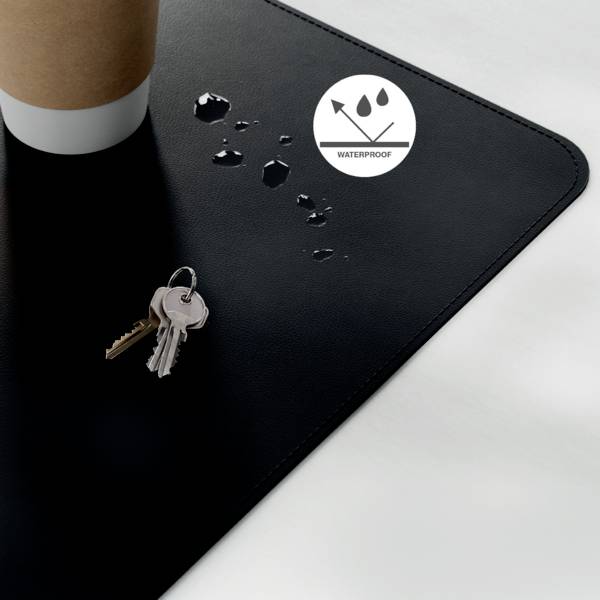A coffee cup sits on a black, waterproof mat, with water droplets forming. Keys are placed nearby, indicating resistance to spills.