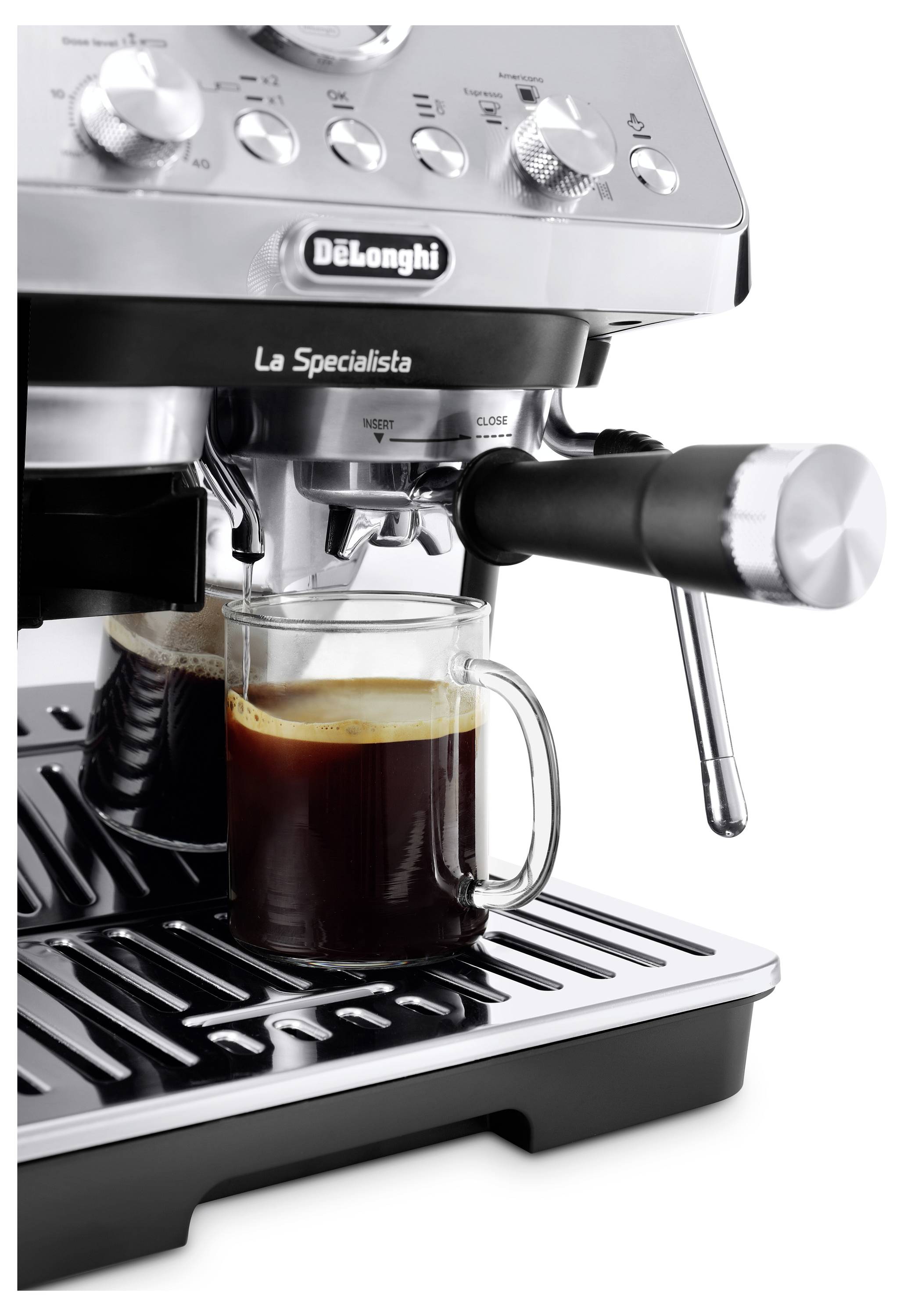 A silver espresso machine with a steam wand and a glass mug beneath, filled with dark coffee, set on a drip tray.