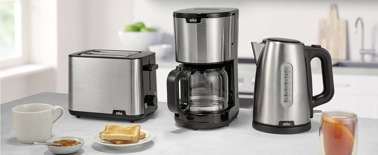 A kitchen countertop displays a silver toaster, coffee maker, and electric kettle. A cup, toast, and a glass of juice are nearby.