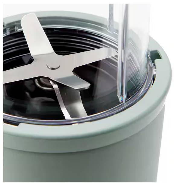 A close-up of a blender's stainless steel blade assembly within a light green base, with a clear plastic lid partially visible.