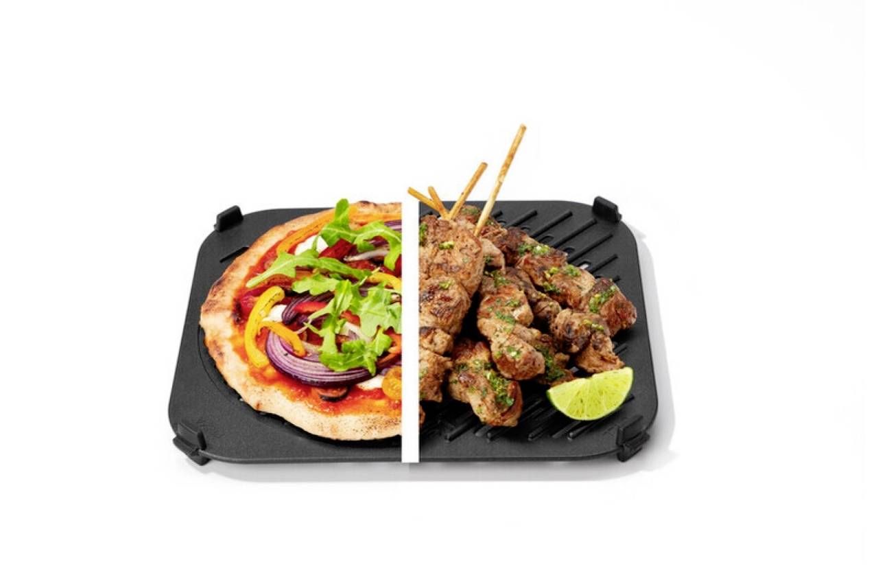 'A plate divided with pizza topped with arugula and peppers on the left, grilled kebabs with lime on the right, over a square grill pan.'