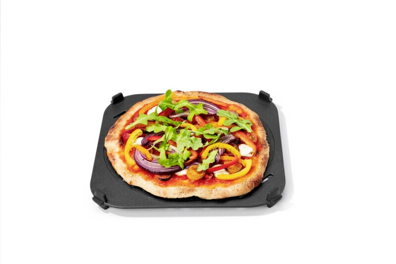 A pizza topped with red onions, yellow peppers, and arugula on a black baking tray against a plain white background.