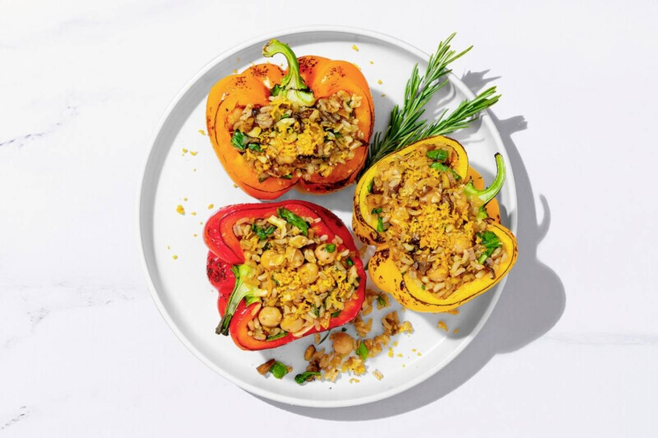 A plate of colorful stuffed bell peppers with wild rice, chickpeas, herbs, and a crunchy topping, garnished with a sprig of rosemary.