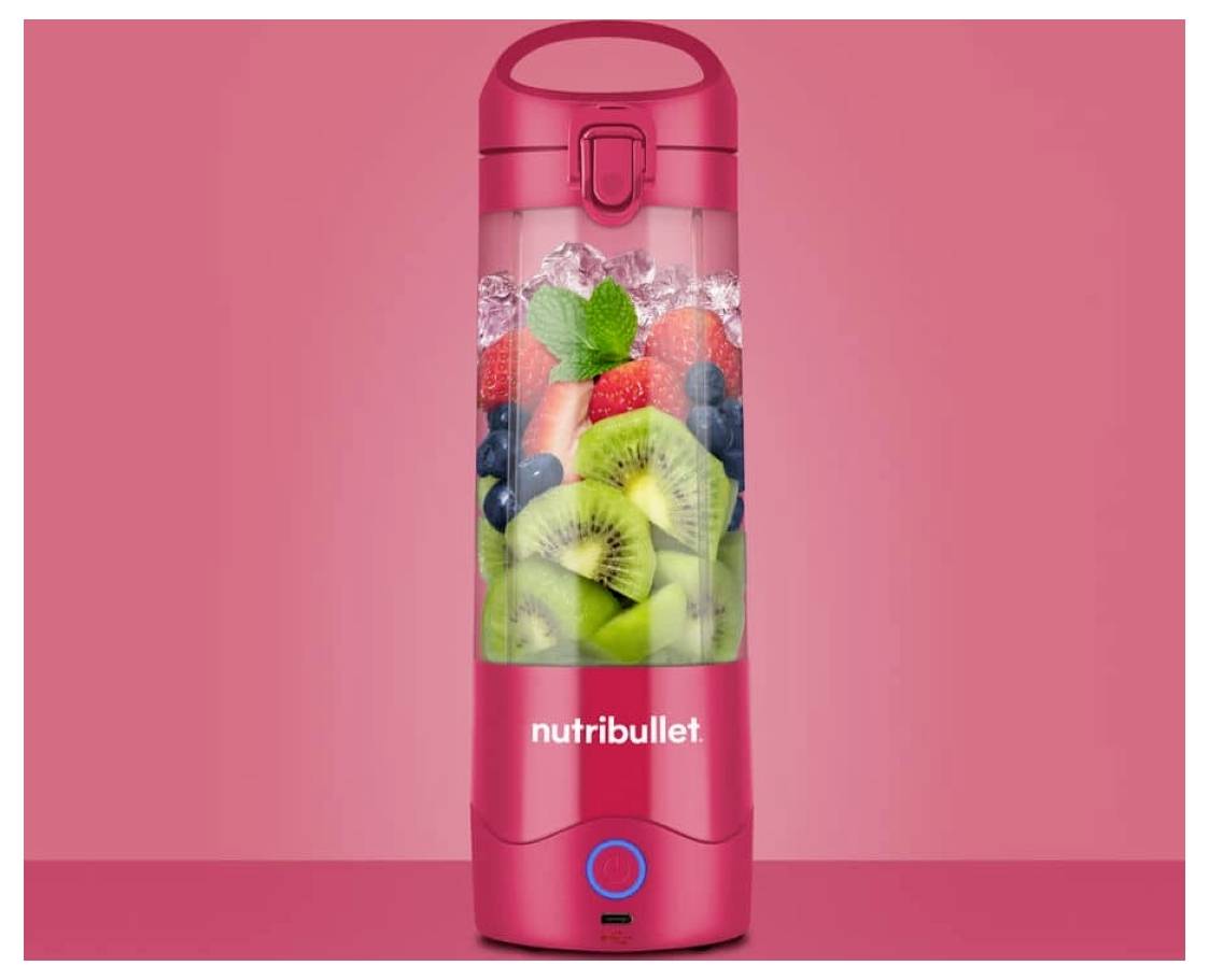 A red Nutribullet blender filled with sliced kiwis, strawberries, blueberries, and mint leaves, set against a pink background.