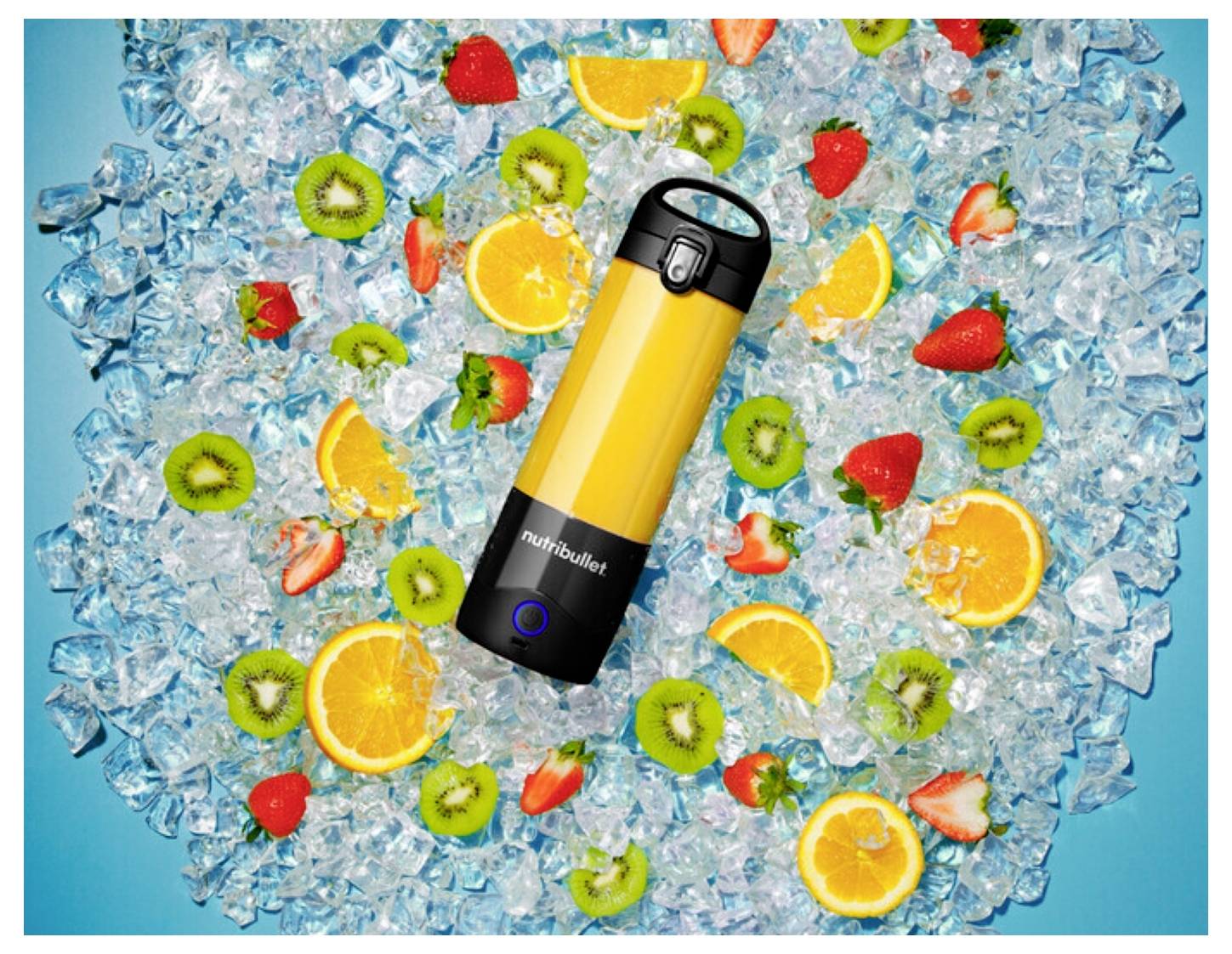 A yellow blender bottle on ice, surrounded by sliced oranges, kiwis, and strawberries on a blue background.