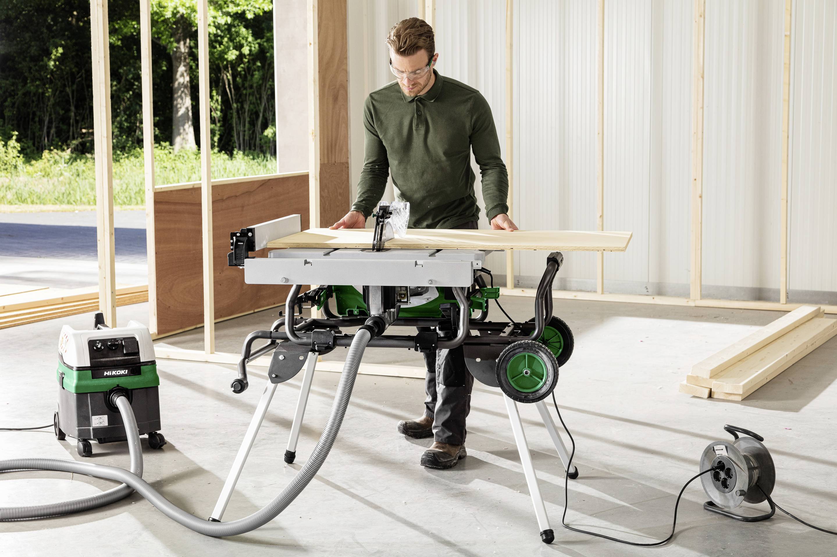 A person stands in a partially constructed building, using a table saw to cut wooden planks. Construction tools are visible around.
