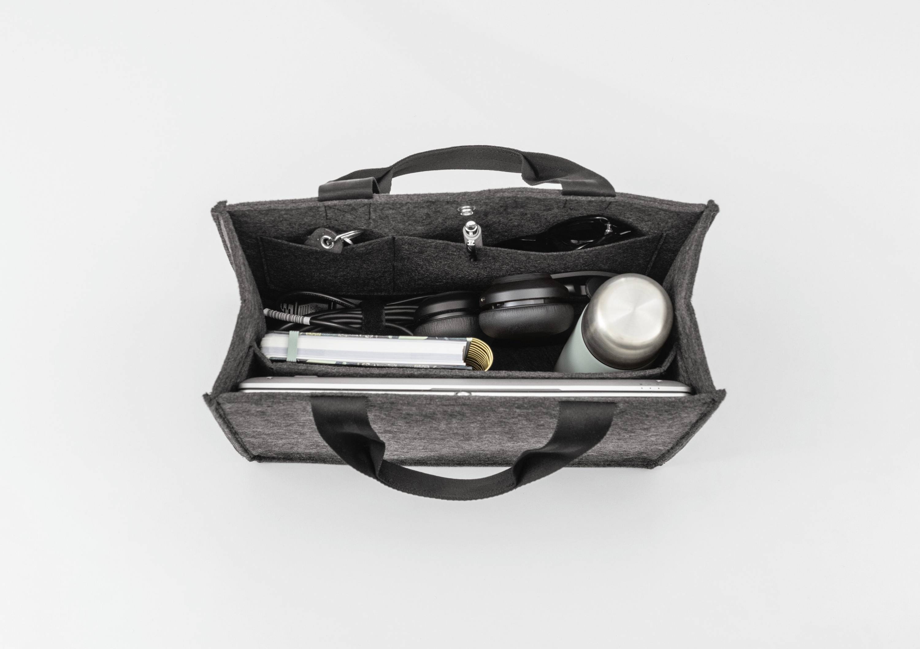 A top-down view of an open gray tote bag with black handles, containing a laptop, headphones, a thermos, and various small items.