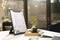 Menu displayed on a black clipboard on a table with a small plant and cup beside it, in a warmly lit cafe.