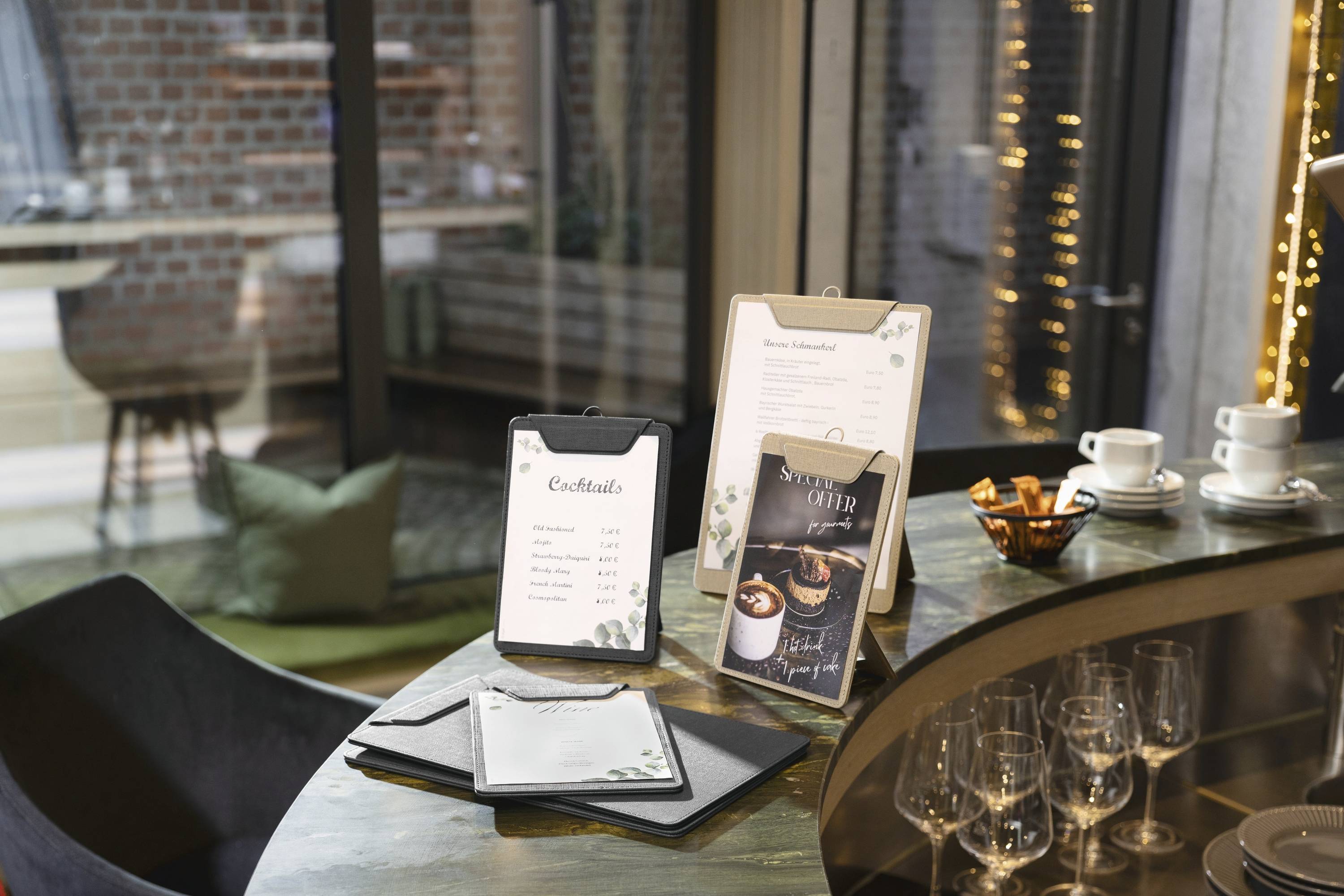 Bar counter with cocktail menus displayed on menu holders, surrounded by empty glasses, plates, and a cozy indoor setting.