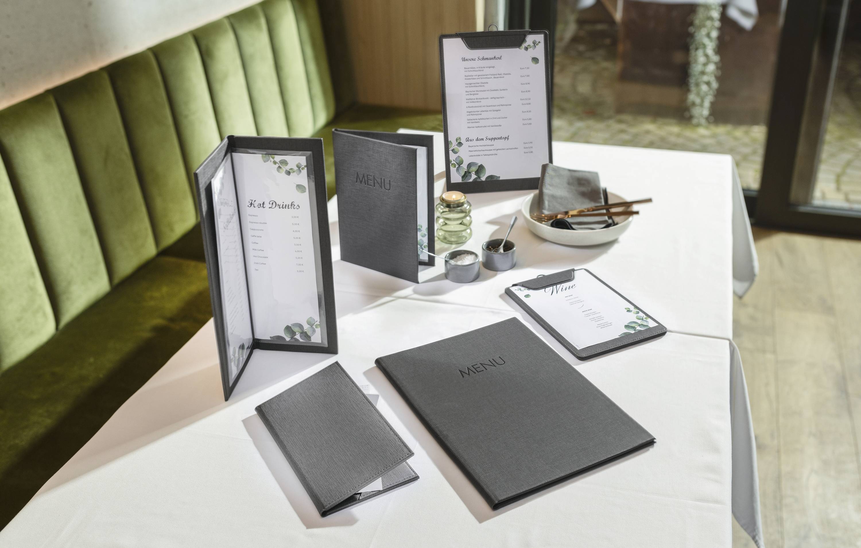 Restaurant table with various menu displays, including a standing menu, closed menu, and clipboard, set on a white tablecloth.