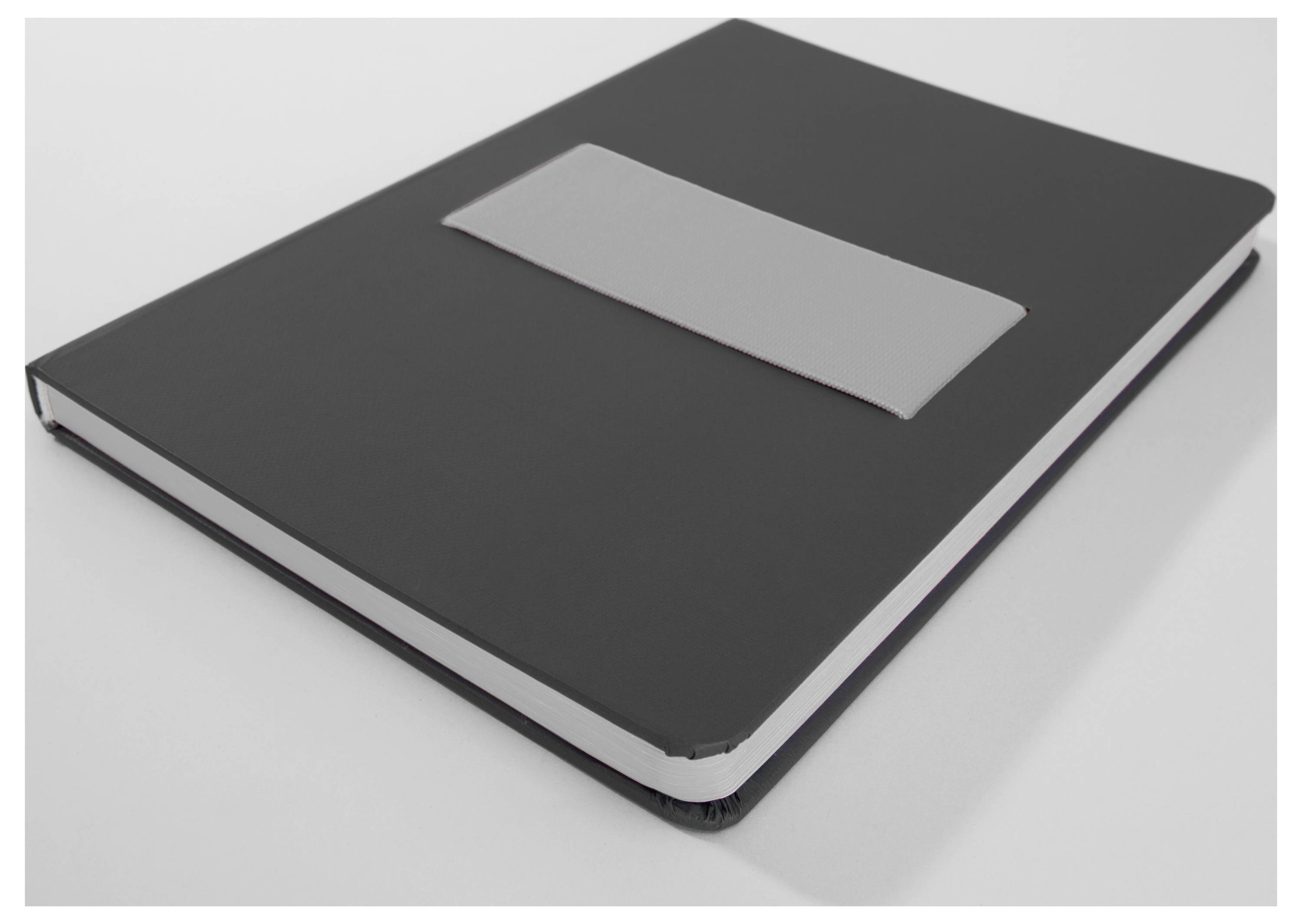 Closed black notebook with a blank gray label on the cover, lying on a light surface.<br>