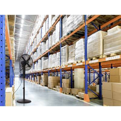 A large warehouse with tall, stocked shelves containing boxed goods. A standing fan is placed on the polished concrete floor near the foreground.