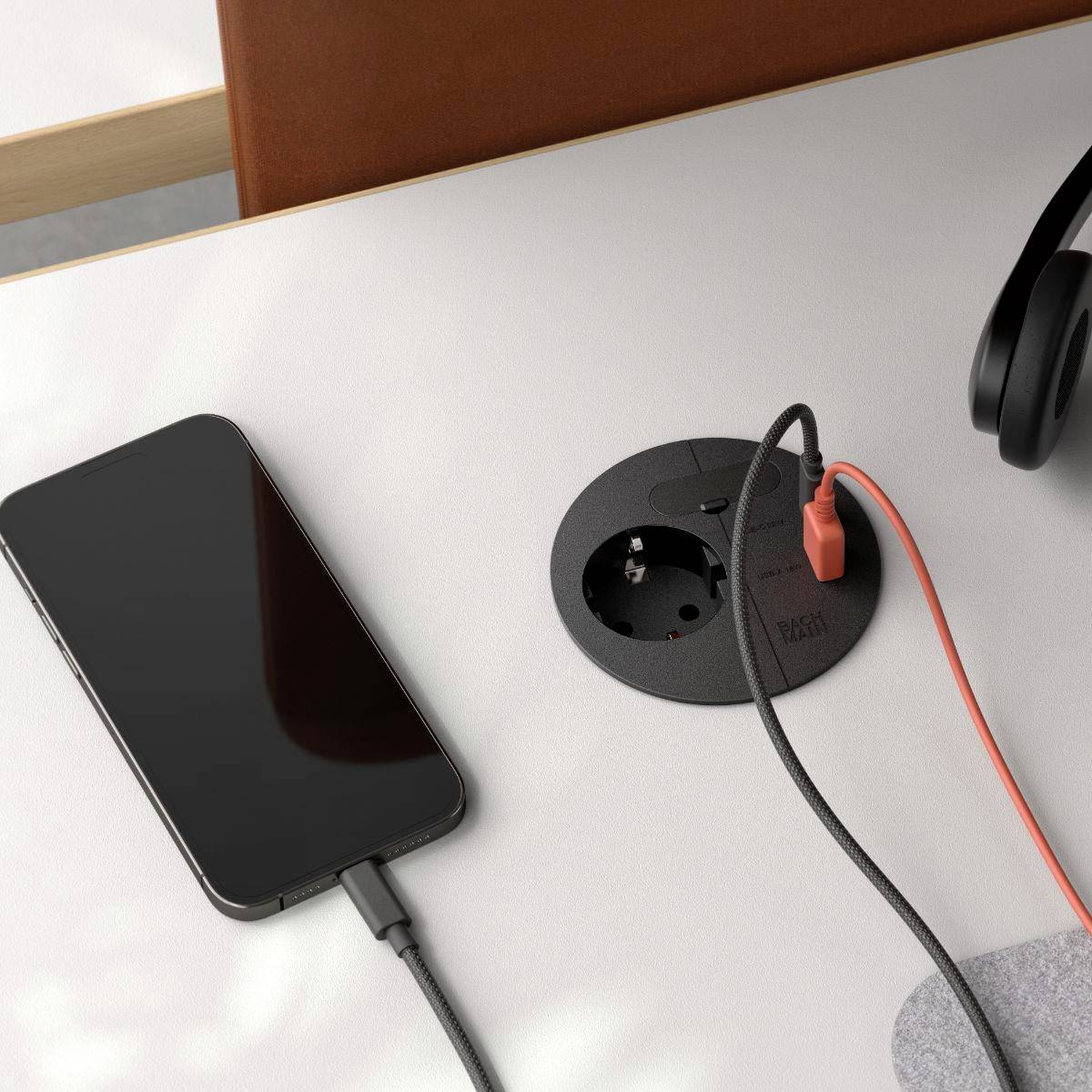 A phone and headphones on a table, with the phone charging via a cable connected to a built-in circular socket.