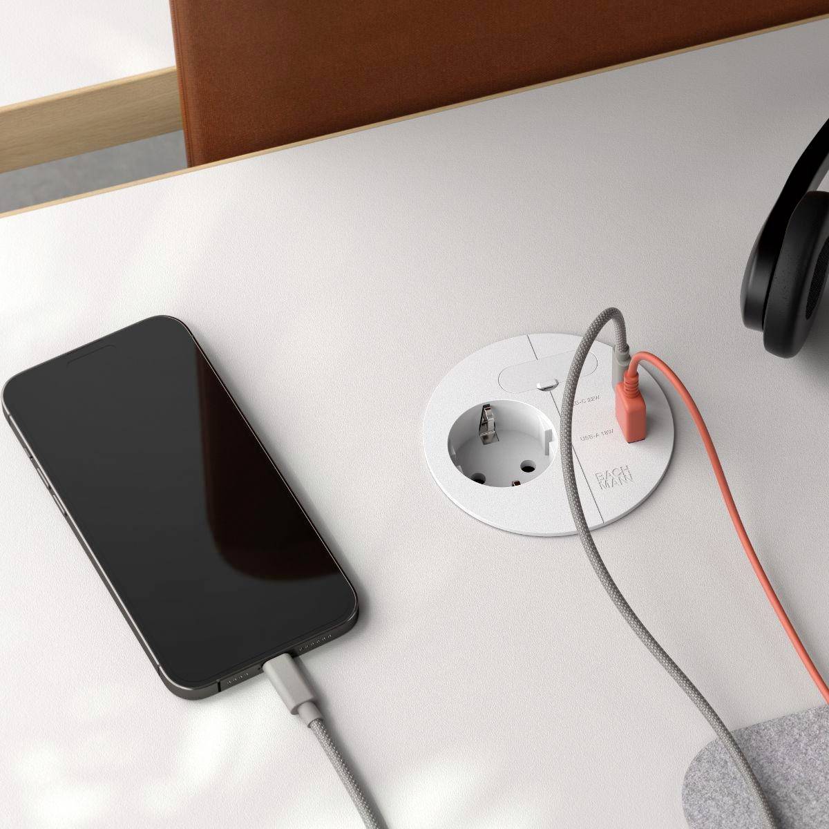A smartphone and headphones connected to a table power outlet; the phone charges via a USB cable, showcasing accessible power solutions.