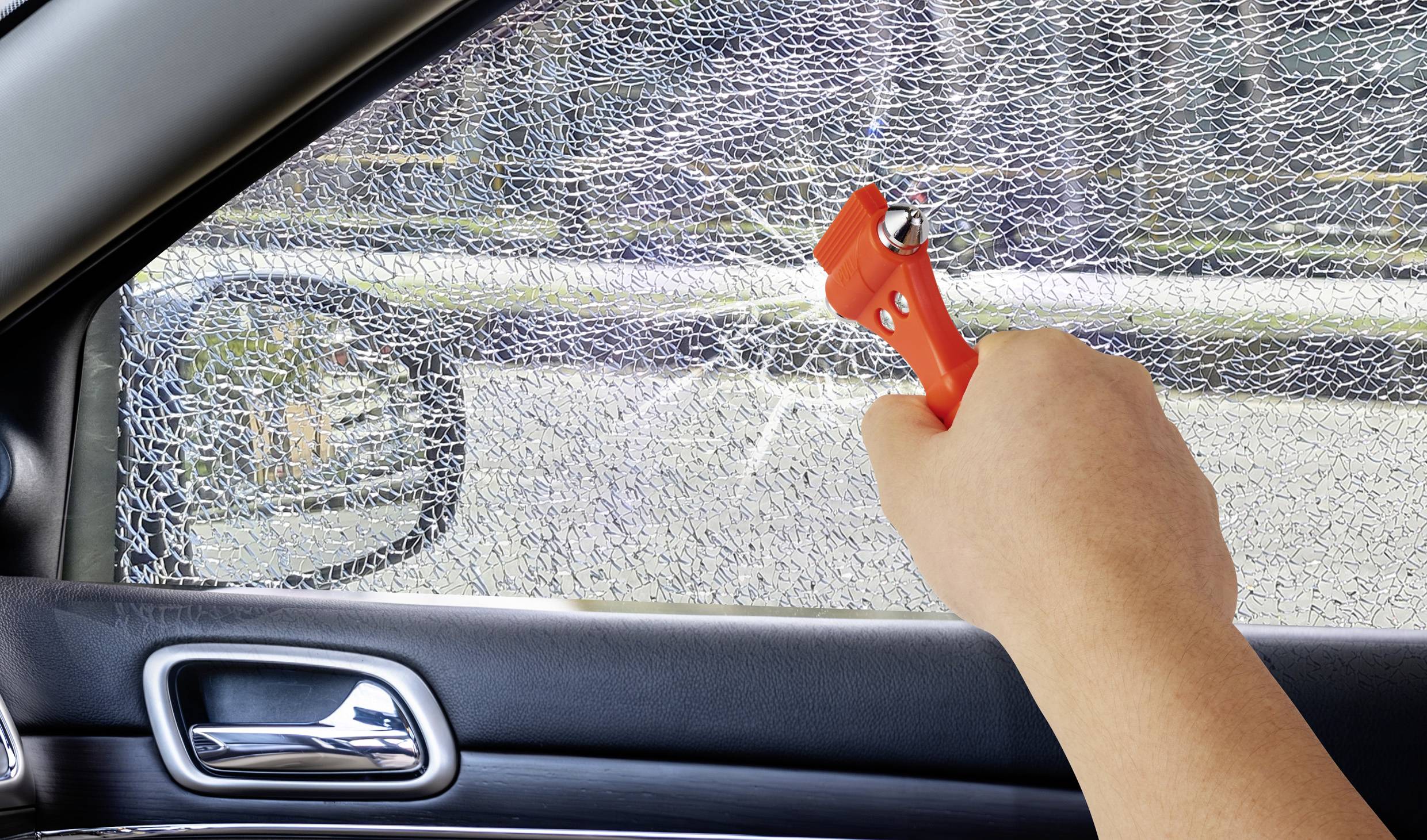A hand uses a car window breaker to shatter a car's side window for emergency escape.
