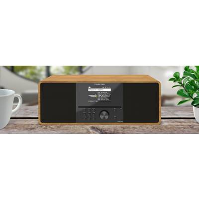 A rectangular digital radio with a wooden frame sits on a wooden table, featuring a display screen, control buttons, and a dial.