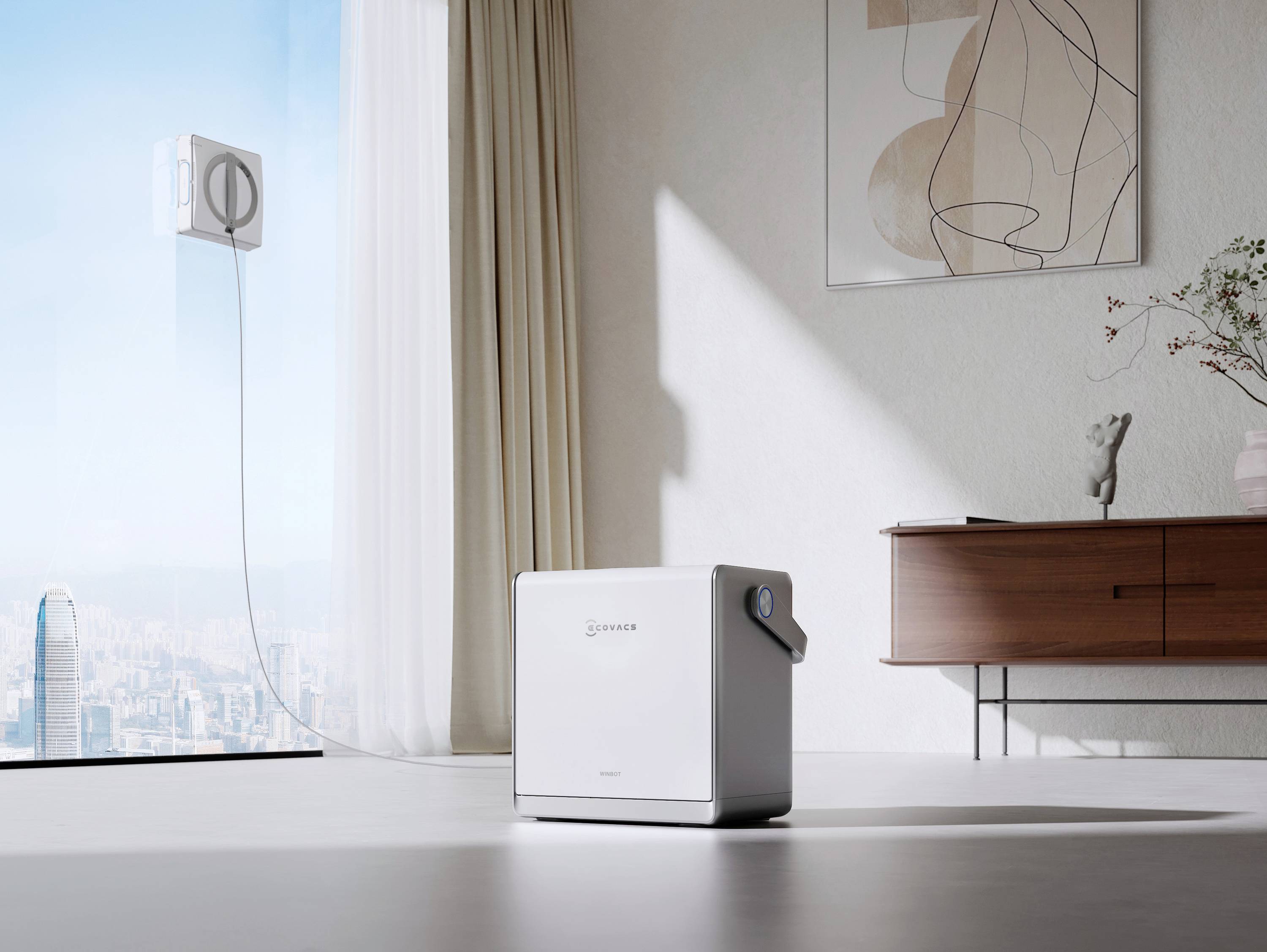 A compact white speaker sits on a minimalist living room floor near a window overlooking a cityscape. Art and a console table adorn the wall.