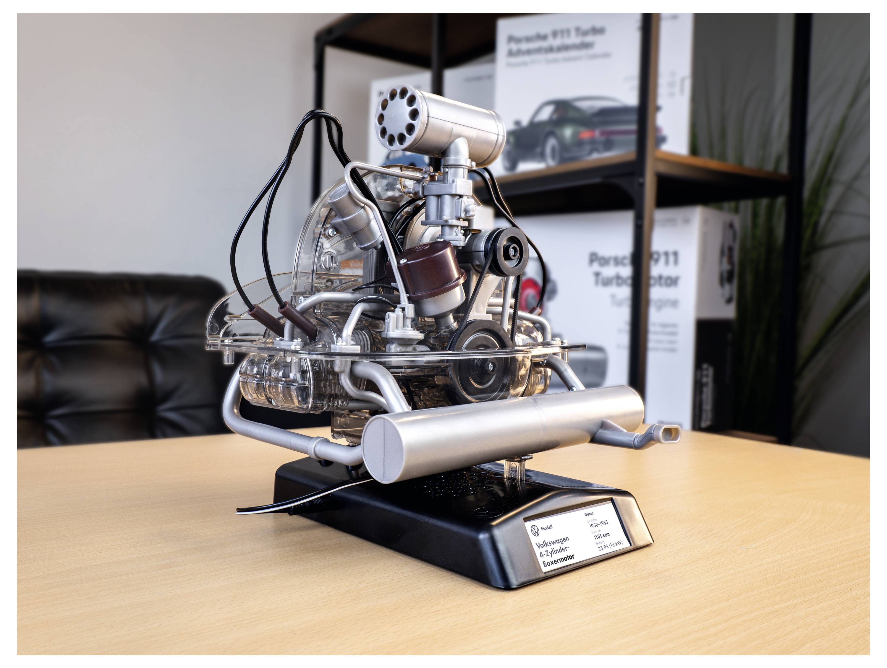 A detailed miniature model of a car engine displayed on a table, showcasing various mechanical components and labeled as a Porsche engine.