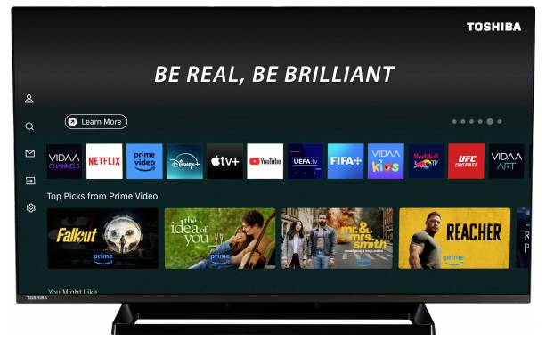 A smart TV screen showing streaming service icons such as Netflix, Prime Video, and Disney+. The top banner reads 'Be real, be brilliant'.