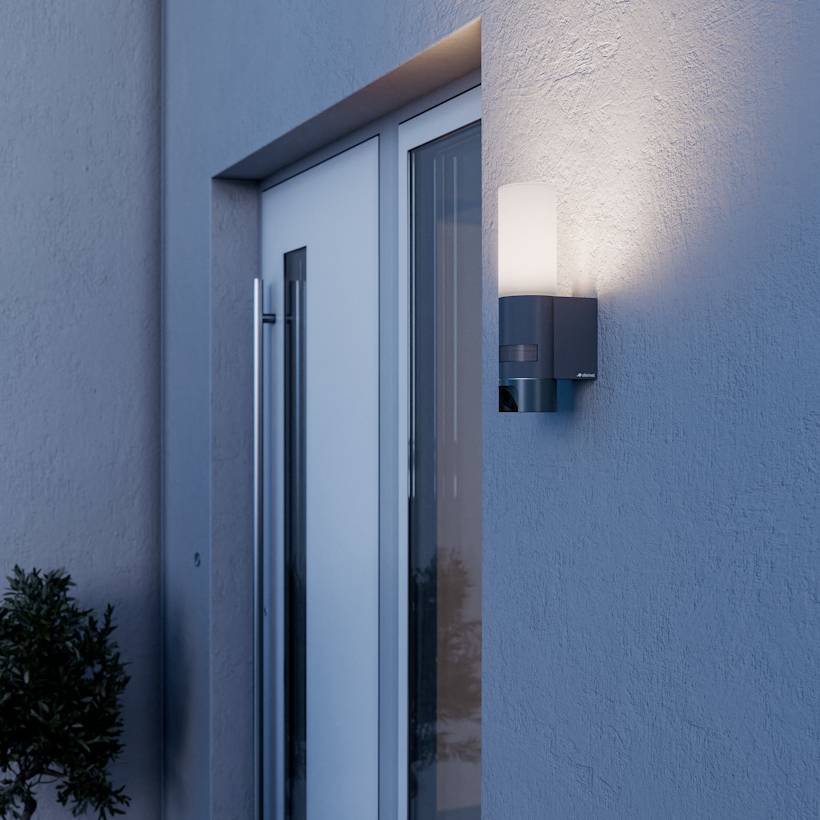 A modern outdoor wall light fixtures a sleek design, illuminating a gray building exterior next to a glass door, adding elegance and safety.