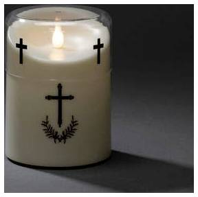 A lit white candle with black cross decorations on its surface, casting a shadow on the gray surface.