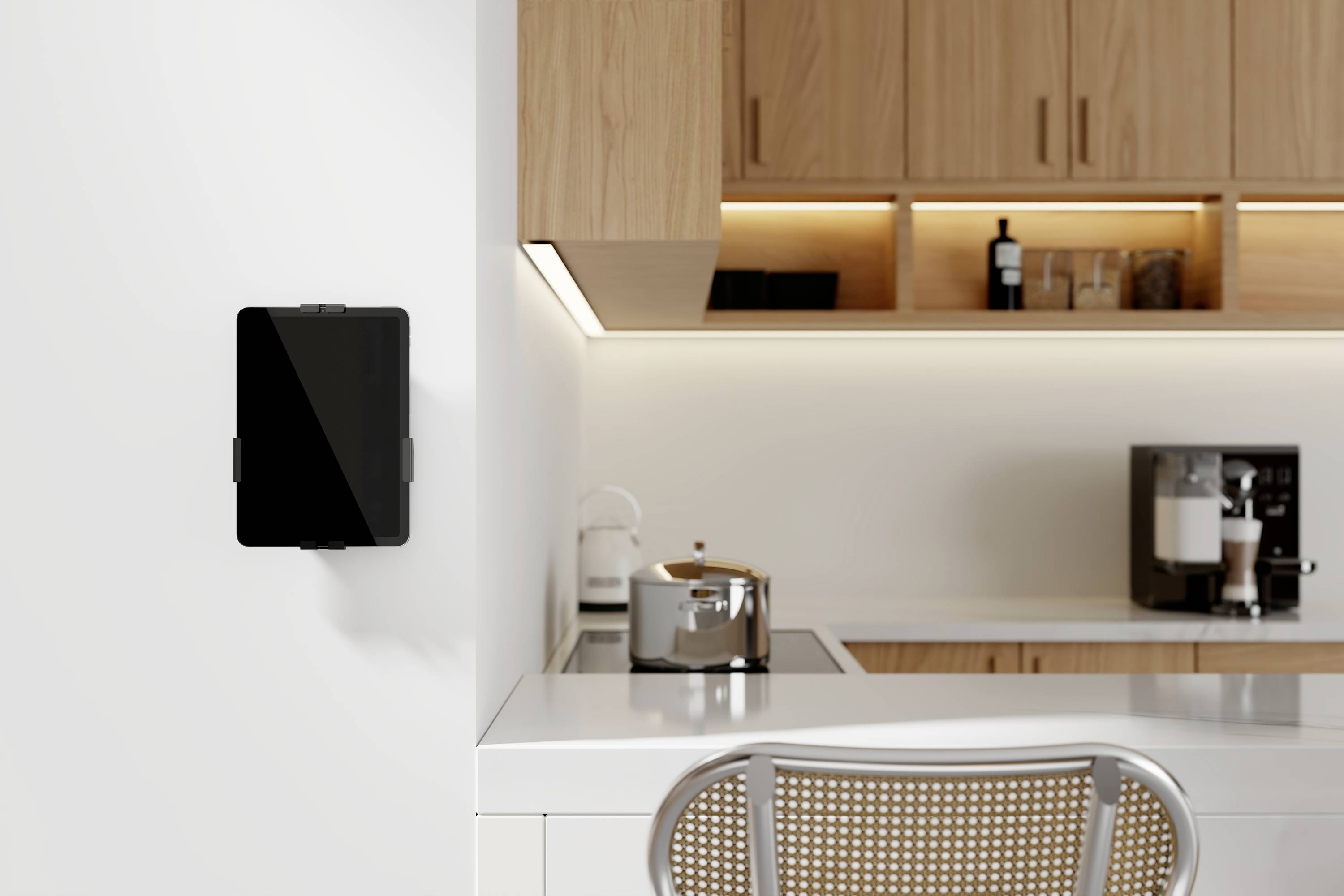 A modern kitchen with light wood cabinets, a mounted tablet on the wall, a toaster on the counter, and a coffee maker in the background.