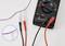 A digital multimeter with red and black probes attached. The dial is set to measure voltage. A close-up shows the probe tips.