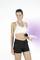 A woman in workout attire uses a handheld massager on her abdomen, standing against a white background.