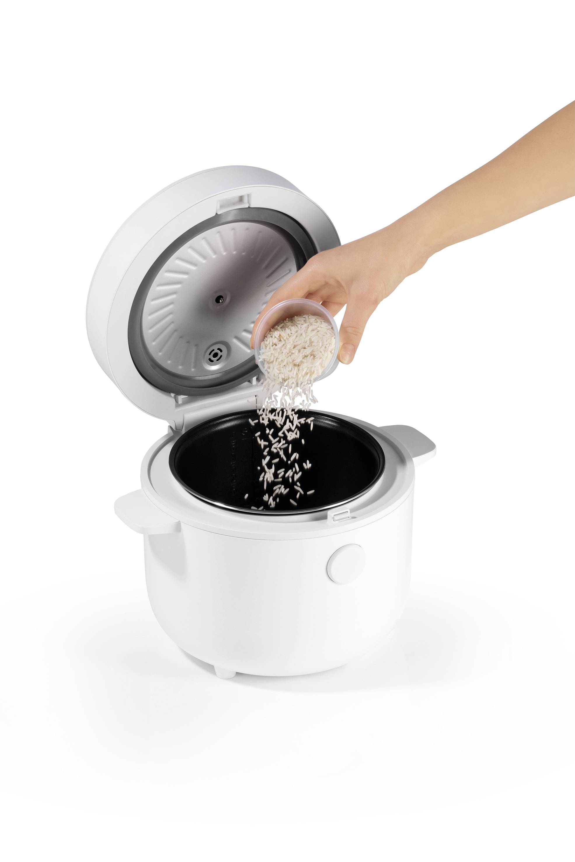 A person pours rice into an open white rice cooker, highlighting the preparation process.