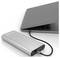 A silver power bank connected to a closed laptop with a black cable, showing charging status lights on the power bank.