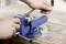 Hands filing a metal block secured in a blue vise on a workbench, with additional metal pieces nearby.