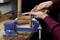A person uses a chisel and mallet to carve wood secured in a blue vise on a workbench, creating intricate details.
