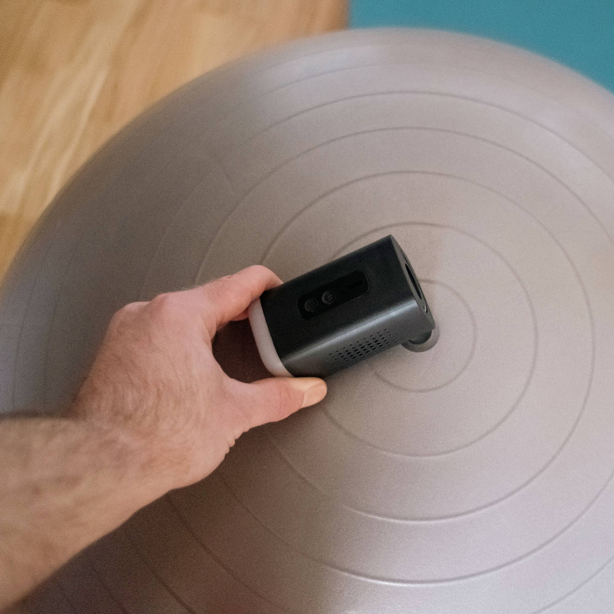 Person's hand holding a small projector resting on a gray exercise ball.