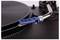 A close-up of a turntable's tonearm with a blue cartridge positioned above a spinning vinyl record on the platter.
