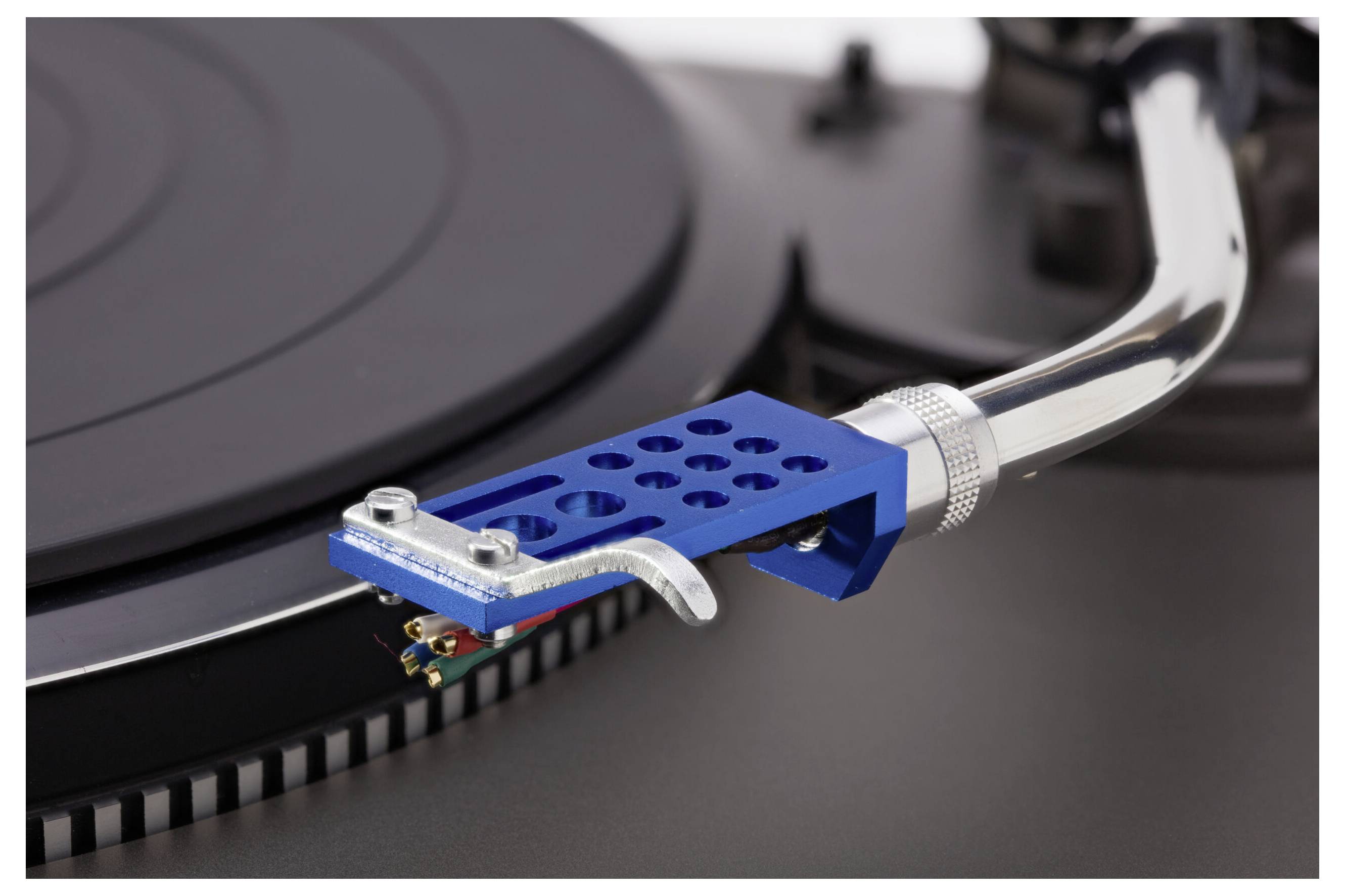 A close-up of a turntable's stylus arm and cartridge positioned over a vinyl record. The stylus arm is metallic with a blue head shell.