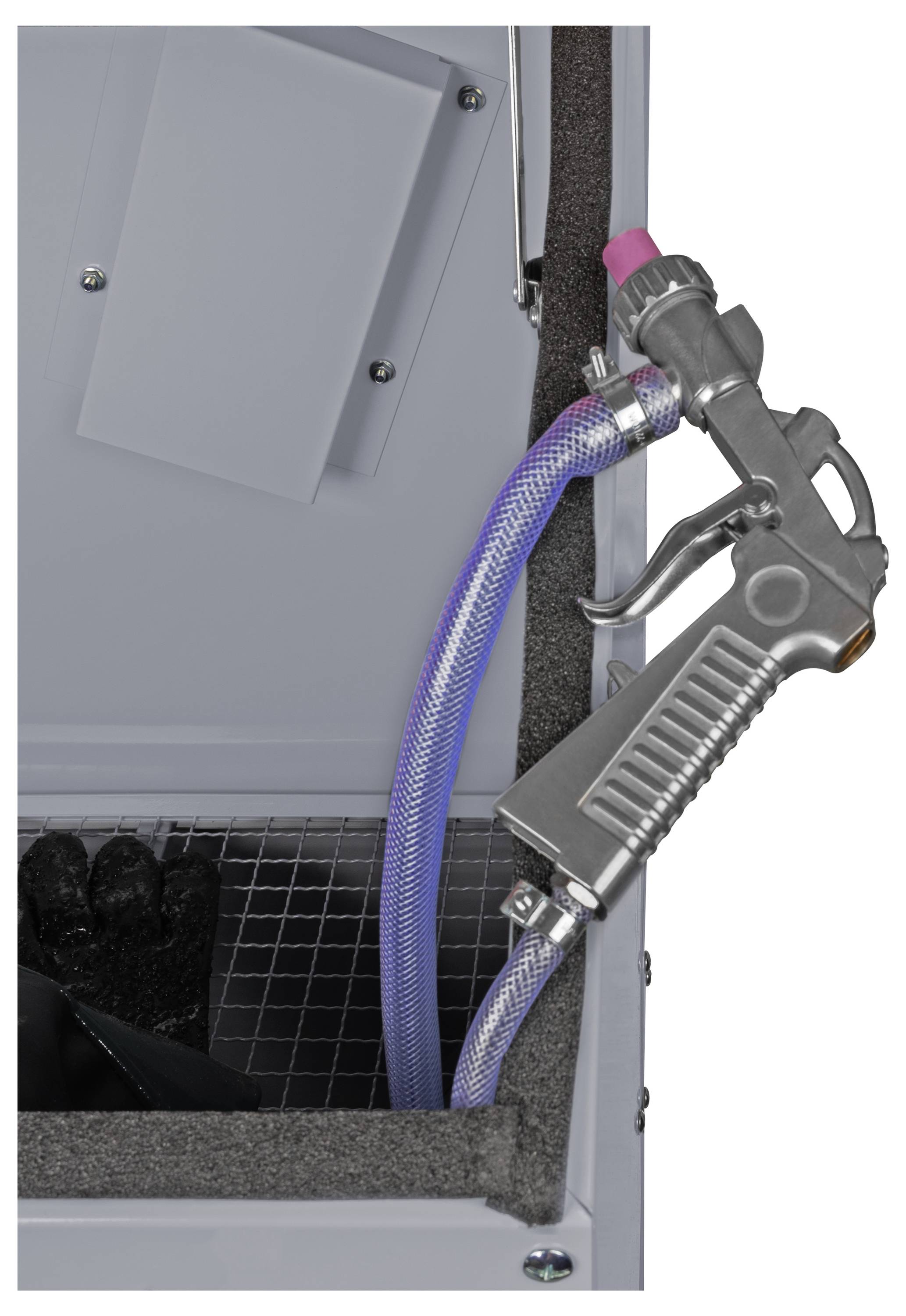 A sandblasting gun and hose are attached to an open sandblasting cabinet, showing a wire mesh surface and protective gloves inside.