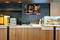 A modern cafe counter with a pastry display case, coffee machine, and digital menu screens overhead displaying various food and drink options.