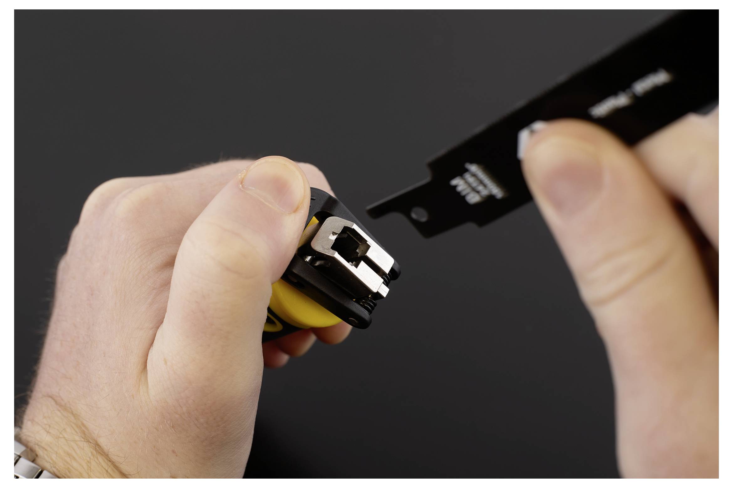 A person inserts a black blade into a yellow utility knife, demonstrating how to change the blade on a black background.
