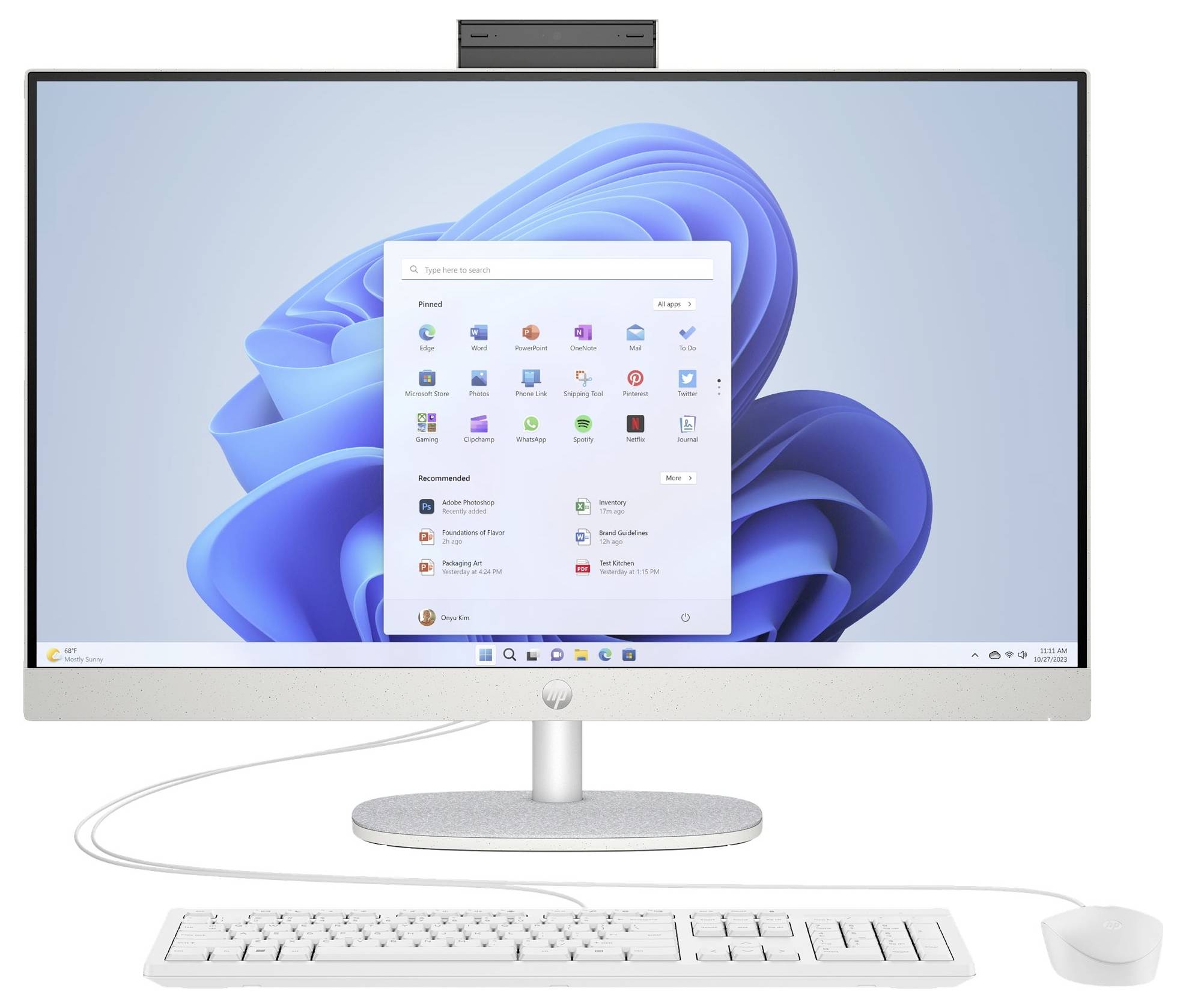 A desktop computer with a large monitor displaying the Windows 11 start menu. A keyboard and mouse are connected below the screen.