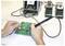 'Hands soldering on a green circuit board with a soldering iron, near a digital soldering station displaying the temperature.'