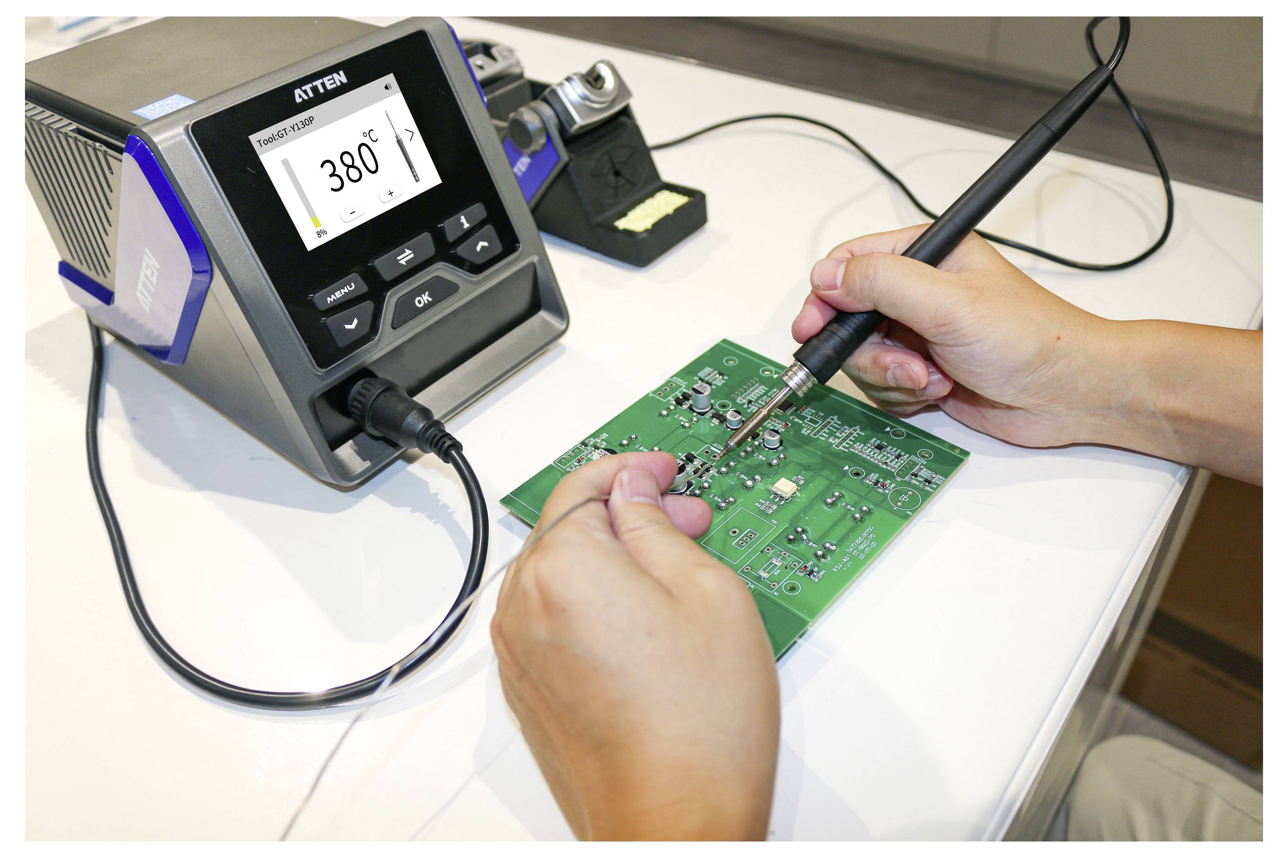'Person soldering components on a green circuit board using a soldering iron, with a temperature-controlled soldering station set to 380°C.'