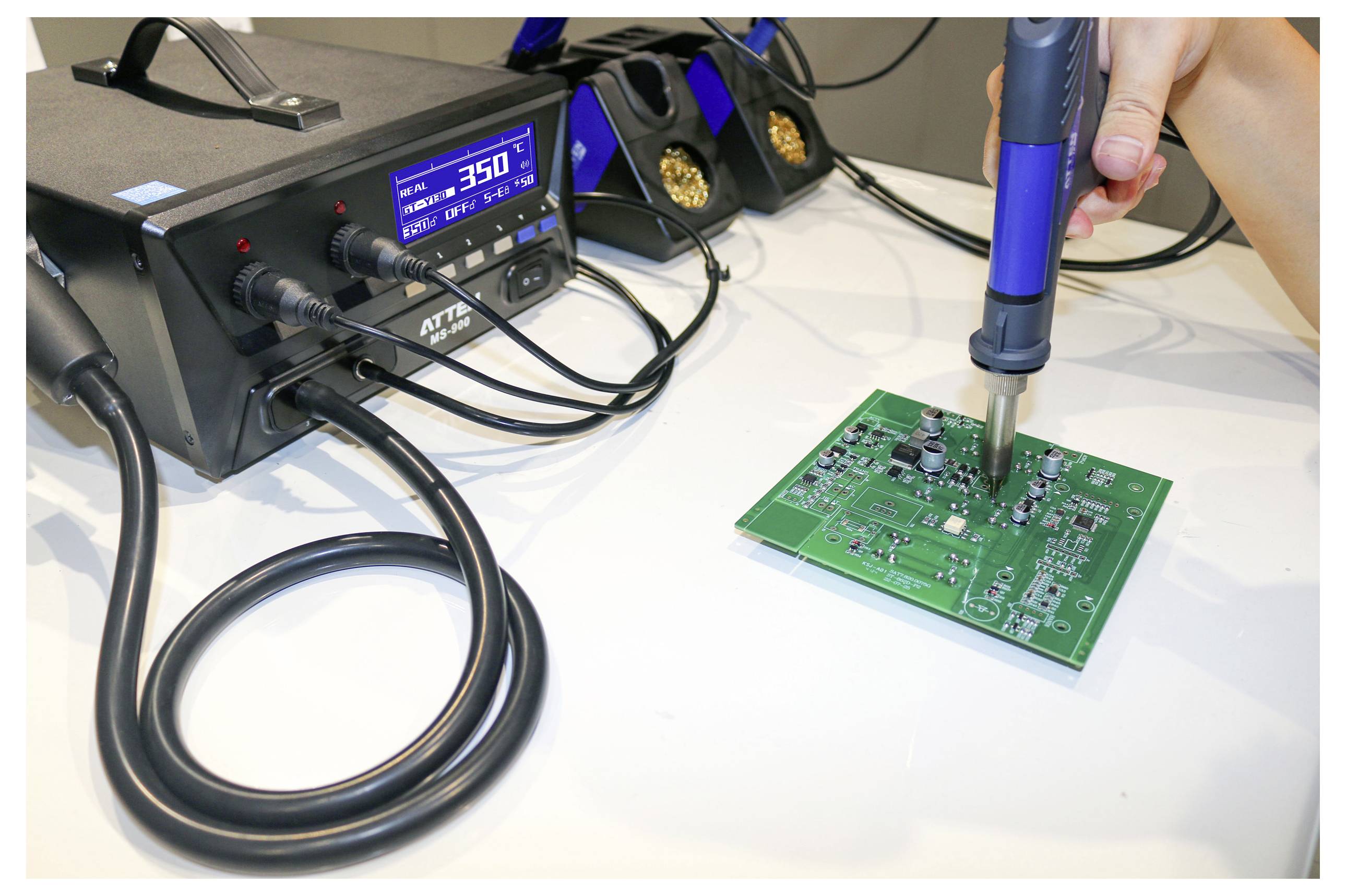 A hand uses a soldering iron on a green circuit board, connected to a digital soldering station displaying a temperature of 350 degrees.