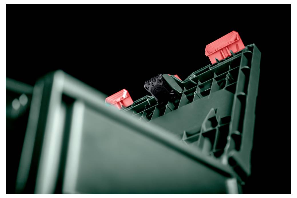 A plastic crate partially open, showing a textured interior and three red latches against a black background.