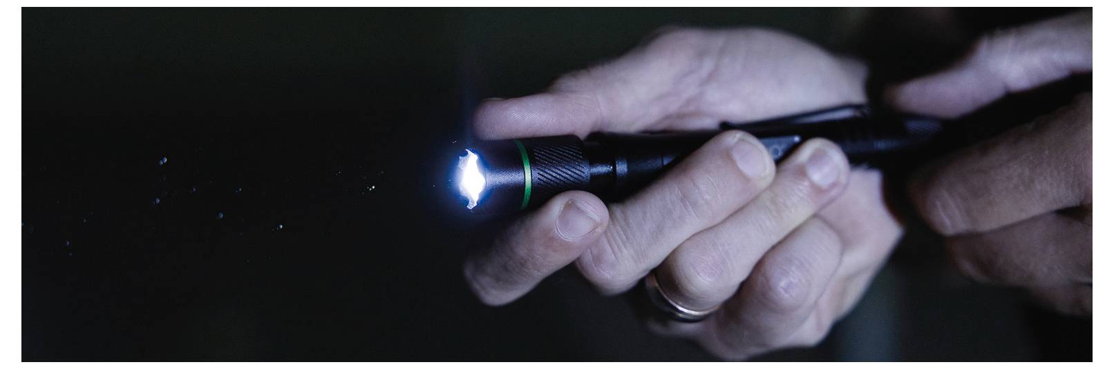 A person holding a small flashlight in the dark, emitting a focused beam of light.
