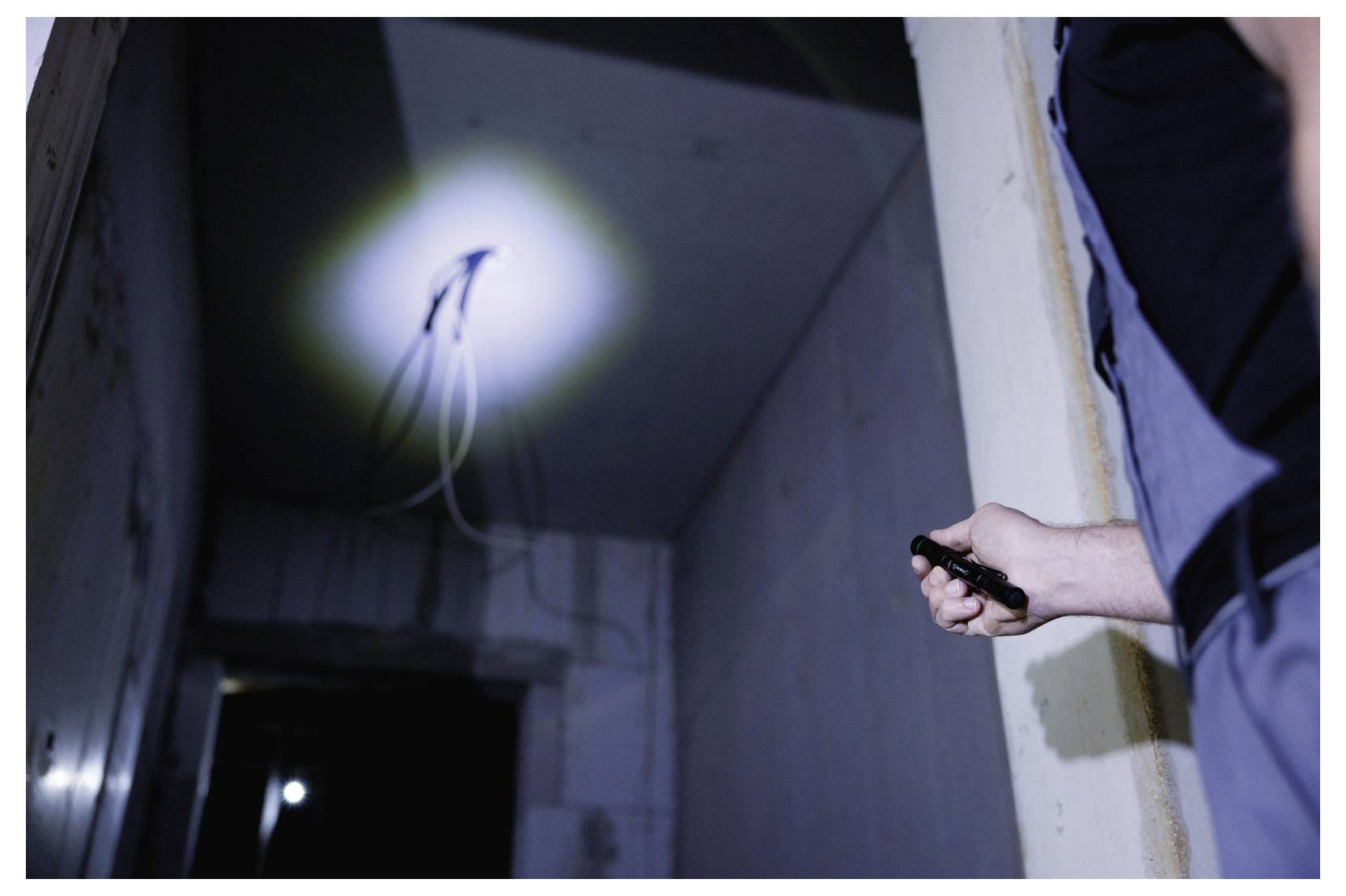 A person holding a flashlight is illuminating exposed wires on a ceiling in a dimly lit room, suggesting an inspection or repair scenario.
