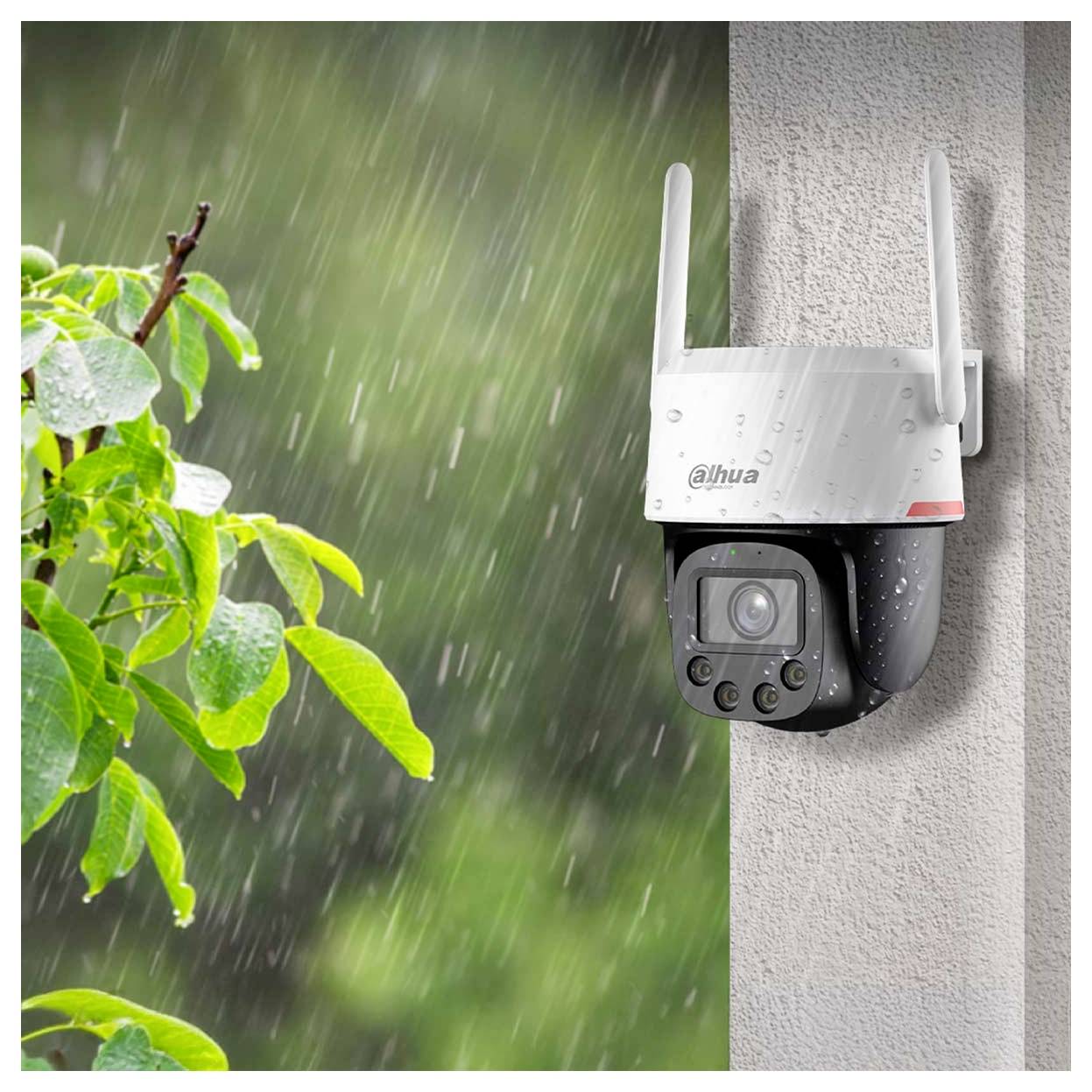 Security camera mounted on a wall under rainy conditions, with green leaves visible. The camera has antennas and a lens facing outward.